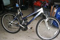 Side view of DBX Resonance trail bike showing blue/white frame, suspension fork, tires, seat, and pedals.