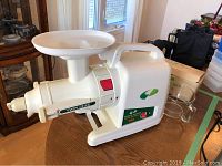 Front angle of Green Power Twin Gear Juice Extractor Juicer showing main body, feeding chute and tray, and clear glass pitcher beside it
