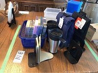 Photo showing 2 steel travel coffee mugs, 2 Nike nylon lunch bags, paper napkins, book stands, small plastic basket, and food storage units on a wooden table.