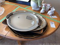 Four stacked serving trays on wood table, showing metal surfaces and handles