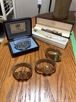 Six wristwatches on wooden surface, three on table and three in boxes, showing variety of bands and dial shapes.