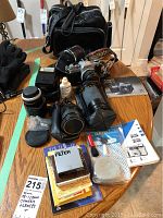 Image showing Canon AE-1 camera with lenses, cleaning supplies, manuals, and black camera bag on wooden table.