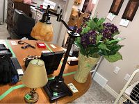 Adjustable table lamp with dark base and amber glass shade, small table lamp with beige shade, and beige vase with faux floral bouquet on wooden surface.