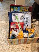 Overall view of the art and writing supplies in a colorful patterned box, showing crayons, pads, pencils, and writing accessories.