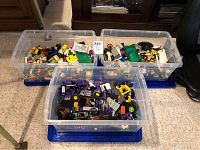 Three plastic storage tubs filled with assorted LEGO pieces in multiple colors and shapes.