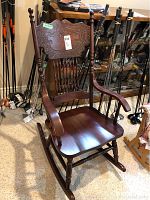 Full view of the dark stained wooden pressback rocking chair with carved backrest and curved armrests.