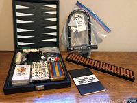 Photo showing the backgammon board open with dominoes, dice cup, dice, playing cards, chess set, and a rules book. Also visible is a wooden abacus and black Norco bike lock in plastic bag.
