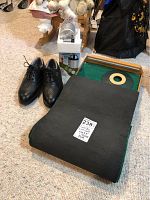 Black FootJoy golf shoes, 8-foot putting mat rolled and flat with a wooden putting hole, and Check-GO sweet spot finder box on carpet.