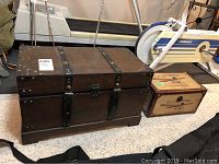 Photo showing both the large dark wood chest with metal straps and the smaller light wood chest with vintage airline labels side by side.