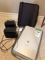 HP Scanjet 4370 flatbed scanner, two black Sony speakers with cables, and a black zippered folder placed on carpeted floor.