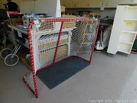 Front angle view of the hockey goal net showing red metal frame and white netting in a garage/storage area.