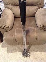 Photo of nine Oscar Jones golf irons standing upright in a recliner chair, showing black grips and steel shafts.