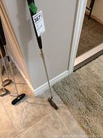Full length view of the golf putter showing metal shaft and grip with green tape at the top, leaned against wall.
