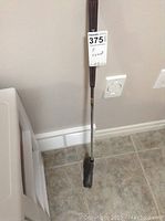 Full view of the TaylorMade golfing putter standing upright showing the grip, shaft, and black putter head on tile floor.