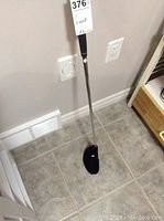 Full view of Carbonite golfing putter standing vertically showing black grip, metallic shaft, and putter head on the floor.