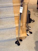 Full view of three Ping golf clubs leaning against wooden stairs, showing shaft and grips.