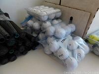 Eight packs of white golf balls in plastic bags and a cardboard box with different brand logos visible on the balls and packaging.