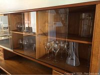 Display cabinet showing multiple pieces of clear glassware including wine glasses and the frosted pitcher.