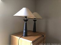 Pair of granite stone table lamps on wooden cabinet, viewed from the side showing both lamps and shades.