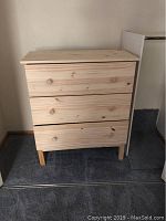 Front view of three drawer dresser made from natural light-colored wood with wooden knobs on drawers and raised legs.
