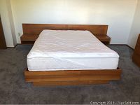 Front view of Scandinavian queen size bed showing mattress and wide wooden headboard with attached nightstands extending from headboard base.