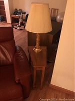 Side table placed beside a leather couch with a lamp on top, highlighting the wood finish and shape.