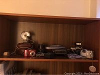 Wide view of shelf showing all items in the collection including cameras, lenses, flash, case, and electronic device