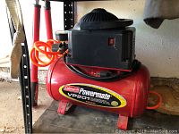 Full view of red Coleman Powermate VP201 air compressor showing motor housing and orange hose coiled on the side.
