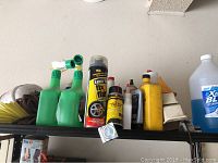 Shelf with various car maintenance fluids and sprays including a large tire fix aerosol can, yellow and clear bottles, and a green trigger sprayer spray bottle