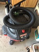 Top view of large black flexible hose coiled on top of red and black Craftsman shop vacuum.