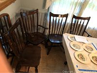Four wooden dining chairs—two captain chairs with armrests and two side chairs—grouped together near a window with sheer curtains