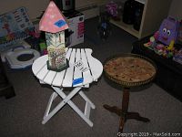 Photo showing white wood folding stand, antique tray stand with marble top, and painted wooden butterfly house placed on and around the white stand in a room corner.