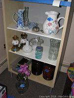 Shelving unit with assorted pitchers, vases, jars, oil lamps, decorative figurines, small lamps, and playing cards.