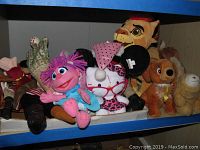 Shelf with assorted plush toys including a pink and blue puppet, black ear plush with pink spots, and brown plush dog.