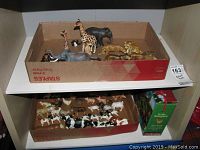 Shelf with two cardboard trays holding jungle animal figurines on top and barnyard animal figurines below, with boxed puzzle on the lower tray.