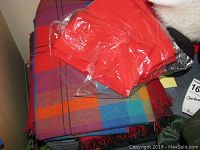Photo of folded colorful plaid fabric with fringed edges and packaged red cloth napkins above