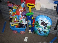 Photo showing a bag of Mega Bloks, small blue wagon with red wheels, a blue toy golf set, a toy megaphone, and a foam wake board with an orca whale design.