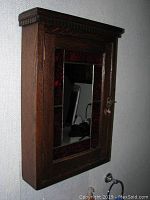 Photo of the vintage oak stained glass medicine cabinet mounted on wall showing beveled mirror door with stained glass border and carved molding top detail, side view showing cabinet depth.