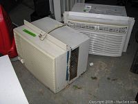 Two window air conditioners (Frigidaire and GE) shown side by side on concrete floor, visible wear and discoloration, showing overall size and condition.