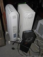 Lot view showing two white oil-filled radiator heaters side by side with power cords visible on the floor.