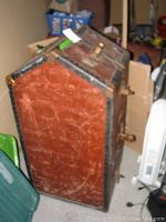 Side view of antique wardrobe trunk showing worn leather surface with cracks and metal reinforcements.