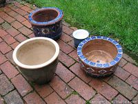 Four outdoor plant pots arranged on brick patio: two terra cotta with blue tile designs, one beige ceramic, one small blue patterned ceramic pot