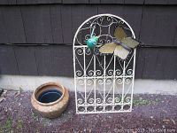 Wide shot showing the ceramic pot placed next to the metal butterfly yard decor leaning against building wall