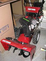 Front-side view of red Craftsman snowblower showing engine, wheels, chute and handle.