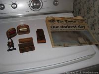 Photo showing six assorted wooden machine pieces displayed on a white surface next to a folded 9/11 Times newspaper.