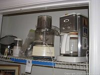 Overview photo showing all kitchen appliances and metal items on shelf including coffee maker, food processor, mini mate chopper, strainer and pot