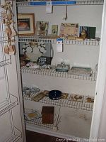 Display of assorted cat-themed decorative items arranged on wire shelves including framed pictures, plaques, dishes, a food bowl, and trivets.