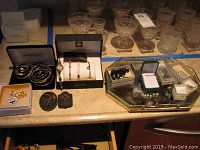 Top view of countertop with jewelry and glassware. Visible Anne Klein watch, gold-tone bracelets, costume pins, black beaded bracelet, and jewelry boxes.