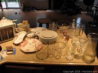 Overall lot of ceramic serving pieces, plates, various glassware, decanters, shot glasses, vases, and trays arranged on table.