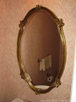 Full view of the ornate gold framed wall mirror mounted on a wall with wallpaper.